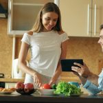 🎬 FULL 4K VIDEO for this still is in my bio link! ⬇️ Attractive couple chatting in the kitchen early morning. Handsome man using tablet while his girlfriend cooking breakfast at home